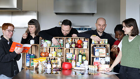Notfallvorsorge & Personen stehen hinter einem Tisch, auf dem viele konservierte und trockene Lebensmittel stehen