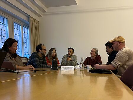 Fachjury Wochen gegen Rassismus Sieben Personen sitzen in einem Halbkreis um einen Tisch herum