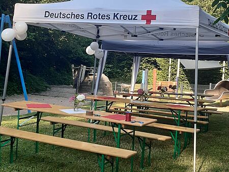 Lummerland Jubiläum Ein weißer DRK-Pavillon, unter dem mehrere Bierzeltgarnituren stehen. Im Hintergrund ist ein Spielplatz zu sehen.