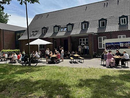 Kita Schatzkistze Menschen an Tischen vor einem Backsteingebäude
