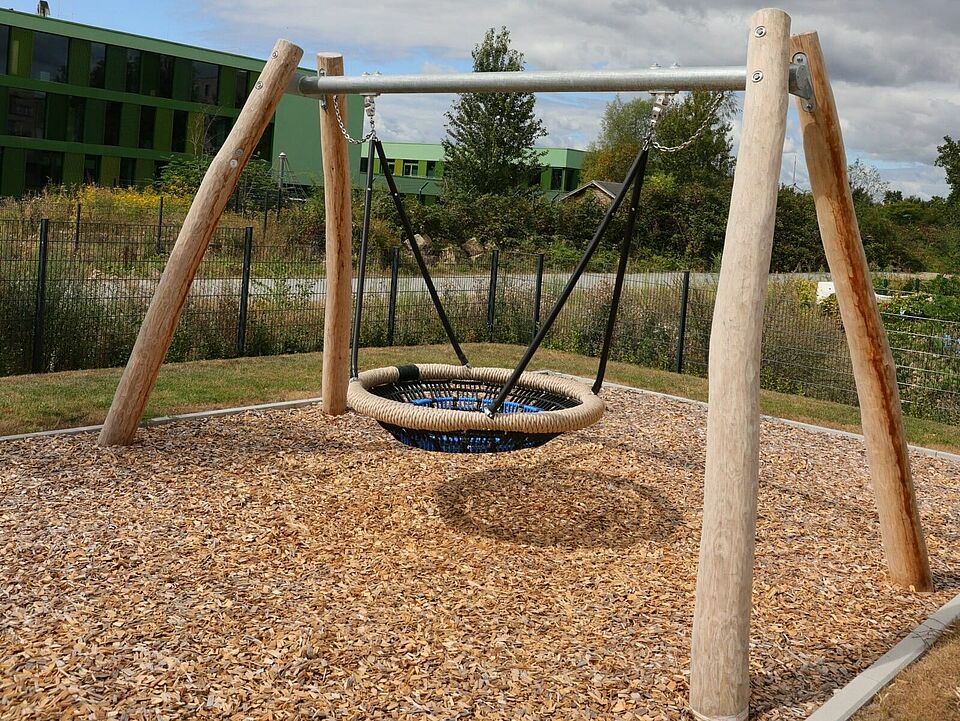 Schaukel Eine blaue Korbschaukel an einem Gerüst auf einem mit Rindenmulch ausgelegtem Platz