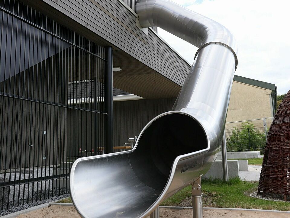 Rutsche Eine silberne Rutsche führt aus dem ersten Stock eines modernen Gebäudes runter auf eine Sandfläche